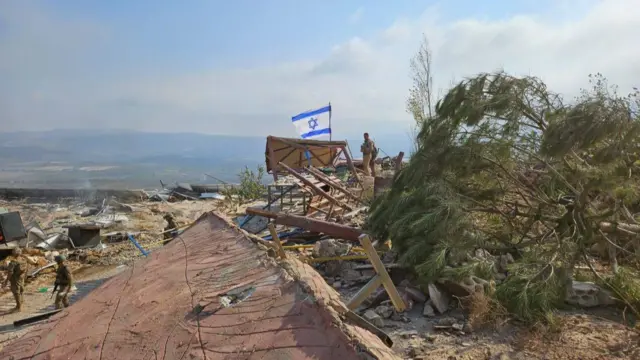 Israeli soldiers raise a flag up among destroyed buildings in Iran Park, Maroun al Ras