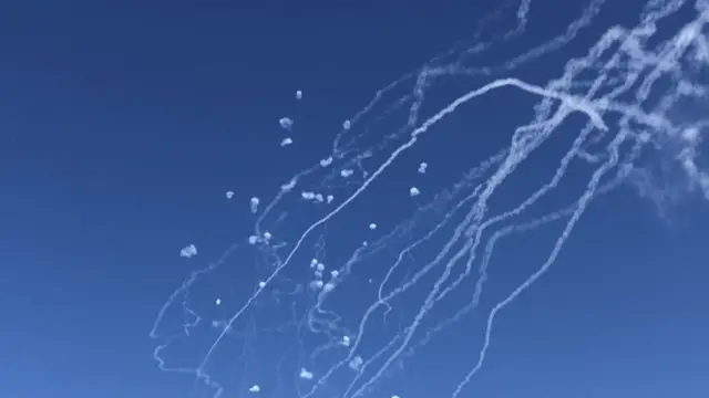 Projectiles are intercepted in a blue sky over Haifa.