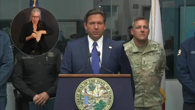 Ron DeSantis at lectern delivers speech. Inset with sign language interpreter to his right and US Army soldier to his left