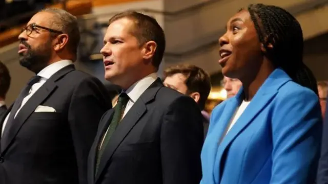 Tory leadership candidates, James Cleverly (left) Robert Jenrick (middle) and Kemi Badenoch sing the national anthem after delivering their speeches at the Conservative Party Conference at the International Convention Centre in Birmingham