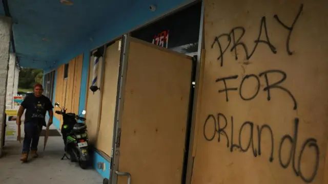 Man walks next to a boarded up building has been graffitied with a message: 'Pray for Orlando'