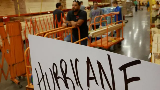 People line up to buy protective wood to before the storm's arrival in Orlando, Florida. A sign that reads "hurricane" can be seen in the foreground.