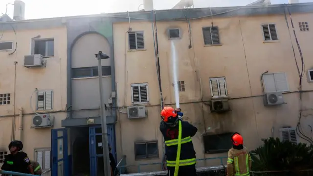 Firefighters battle a fire in a residential building in Kiryat Shmona that is tinged with soot and smoke