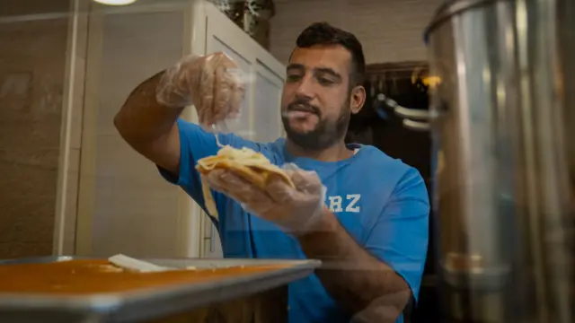 A man wearing a blue t shirt prepares dessert kunafeh