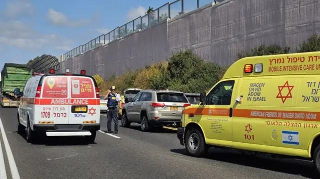 Two ambulances on a road with a police officer standing beside one.