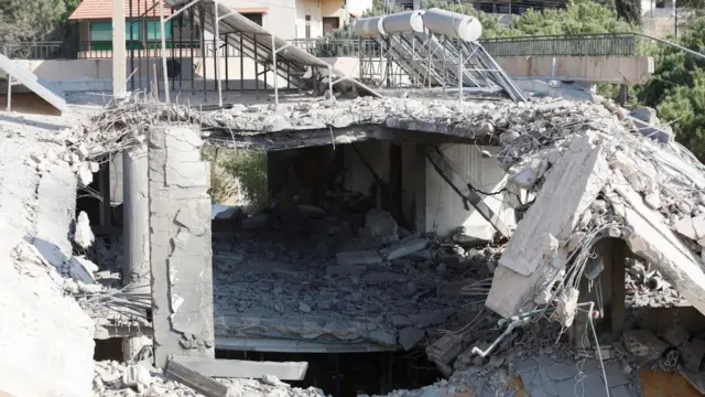 Rubble of a building can be seen, with exposed concrete, rebar, and debris spread on the ground.