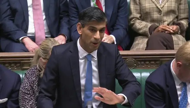 Rishi Sunak in dark blue suit and light blue tie stands in Commons asking question to Starmer