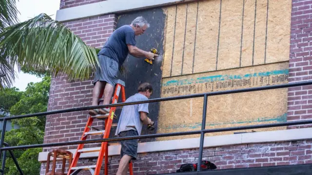 Two men with drills boarding up a building with wood in Florida ahead of Hurricane Milton