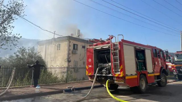 A fire engine and firefighter with smoke billowing in the background