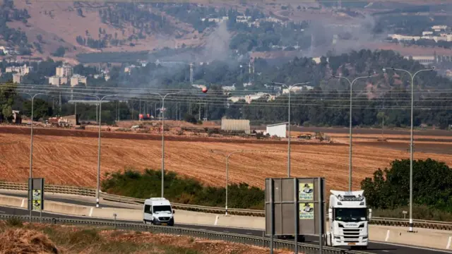 Smoke rises from Kiryat Shmona, next to a road as traffic passes