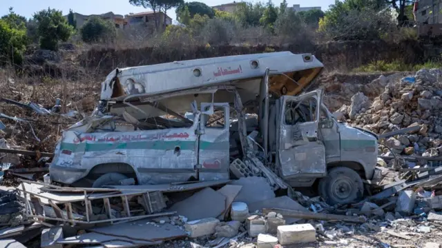 An ambulance is crumpled and crushed under rubble and dust