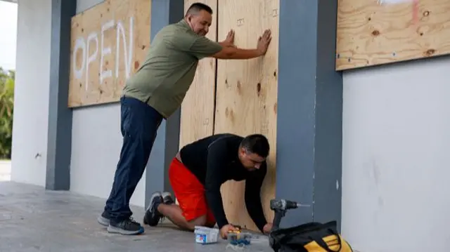 Two men, Salvador Gonzalez and Jorge Leon, place plywood over the windows of a business in Fort Myers.