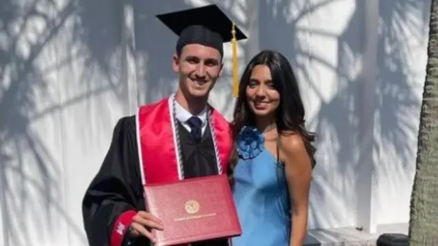 Jay Skelcher-Maxwell wearing a graduation cap and gown alongside his partner.