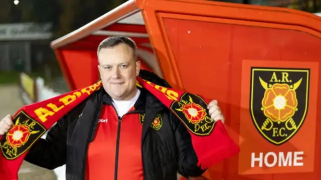 Albion Rovers fan Duncan McKay poses in the team's dugout with a scarf as he prepares to manage the team for a one-off game