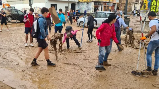 People cleaning a muddy street with brooms