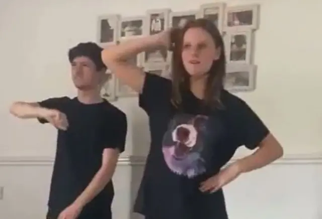 MacPhail, in a black t shirt, and Holly, in a black t shirt with a dog on the front, perform dance moves together in a living room