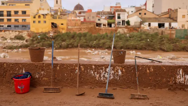 Brooms and buckets leaning against a wall surrounded by mud