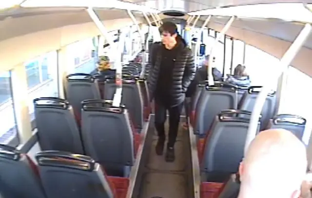 CCTV still of MacPhail walking along the aisle of a bus. He is dressed all in black