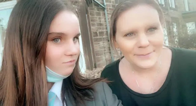 Holly takes a selfie with her mum. Holly has long dark hair and Micala blond hair. They are outside a house