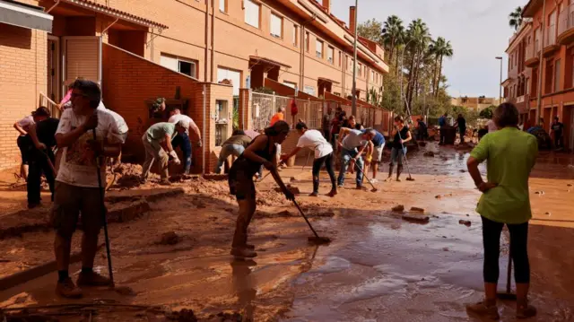 A group of people sweep thick brown mud from a street