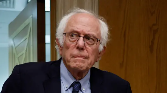 Bernie Sanders, with white hair and black glasses and wearing a suit