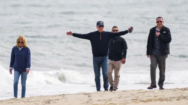 U.S. President Joe Biden gestures as he and first lady Jill Biden walk on the seashore in Rehoboth Beach, Delaware