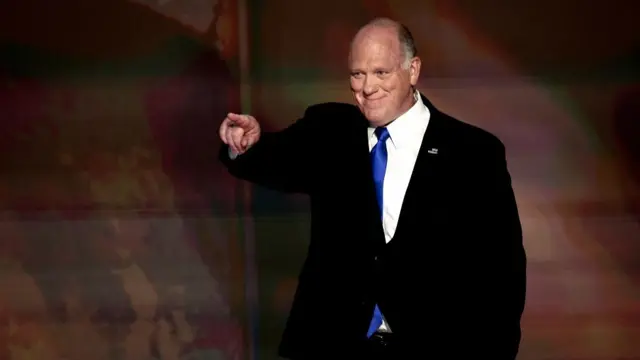 Homan on stage at a Republican convention pointing at the crowd. He's wearing a black suit and blue tie and is smiling
