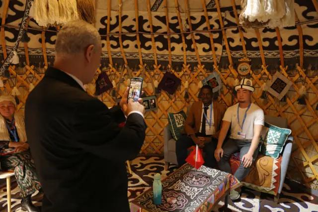 Visitors snap photos inside a yurt at the Kyrgyzstan pavilion. A man takes a picture of them