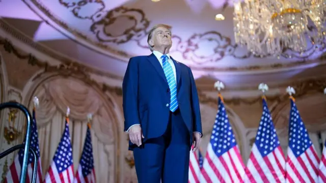 Donald Trump, taken from below, at Mar-a-Lago with American flags behind him