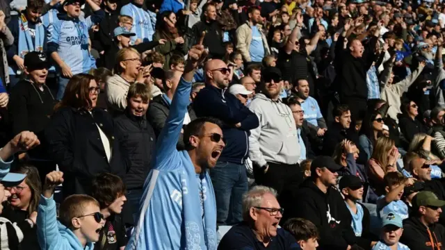 Coventry City fans in the stand, some shouting or chanting loudly