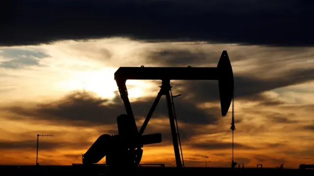 An oil rig is seen in a field and the sun is setting with a dark sunset looming.