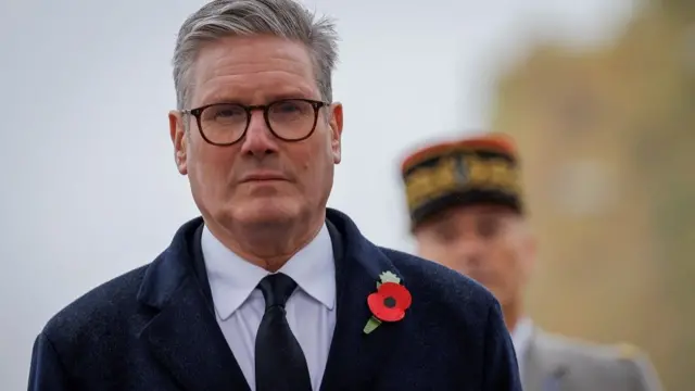 Starmer looks solemn as he stares at the camera. He's wearing a remembrance day poppy