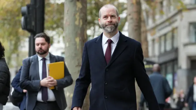 Jonathan Reynolds walking wearing a suit