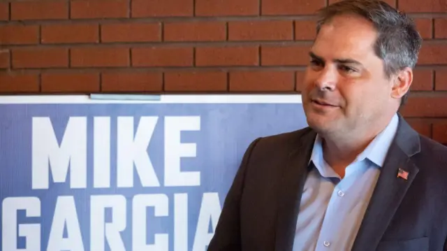 Mike Garcia stands in front of a campaign banner bearing his name.