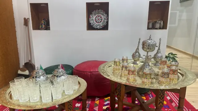 Tea pots and glasses sit on small gold tables