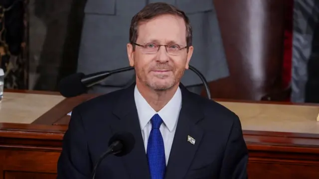 Isaac Herzog wearing a dark blue suit, blue tie and white shirt. An Israeli flag badge is pinned to his lapel.