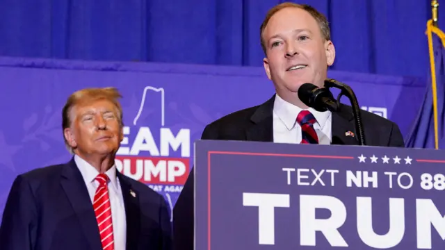 Donald Trump watches Lee Zeldin who is standing at a lectern speaking at a rally,