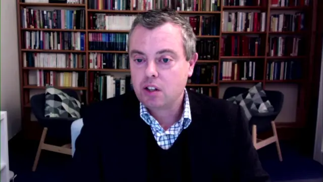 Headshot of Howles talking. He is sat in front of a bookcase