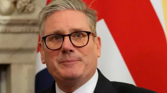 UK prime minister Kier Starmer is pictured against the British flag. He is wearing a suit and thick-framed glasses.