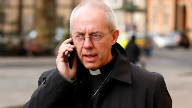 Justin Welby walking the street holding a mobile phone to his ear