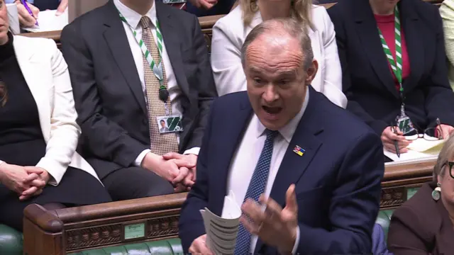 Ed Davey stands with mouth open mid-sentence as he holds some papers while speaking at PMQs