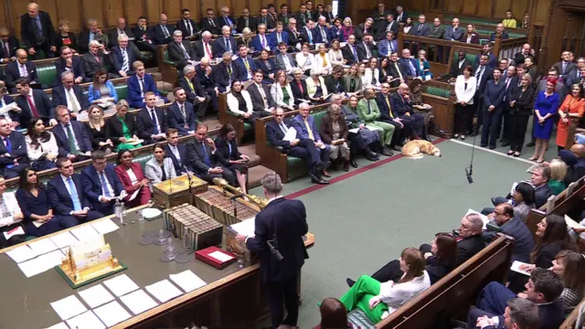 Starmer stands with his back to the camera in the centre of the commons as he addresses Badenoch and MPs opposite him