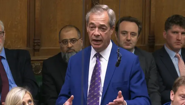 Nigel Farage wears a blue blazer, white shirt and purple tie as he gestures with his hands while speaking at PMQs