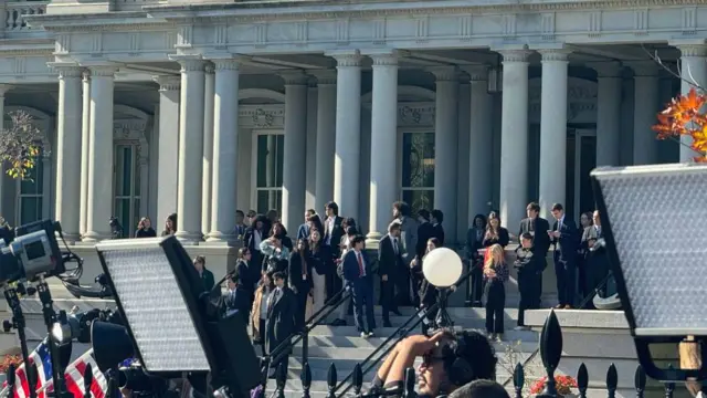 People and press gather outside the White House with cameras