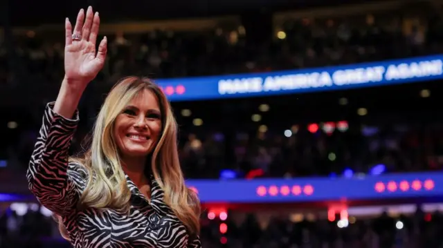 Melania Trump smiles and waves her hand.