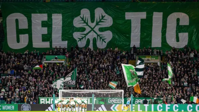 The Celtic squad huddle together in front of a large Celtic banner during a UEFA Women's Champions League match between Celtic and Chelsea at Celtic Park