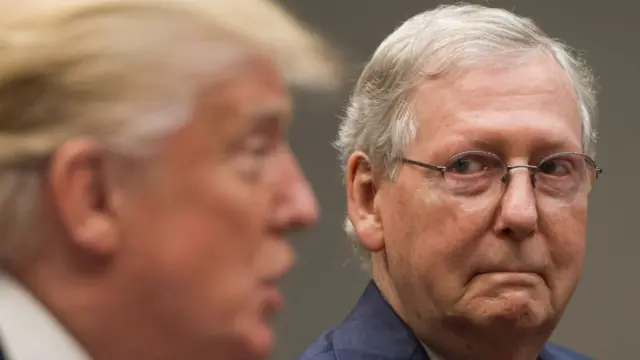 Mitch McConnell (right) looks on as Donald Trump (left) in the blurred foreground speaks