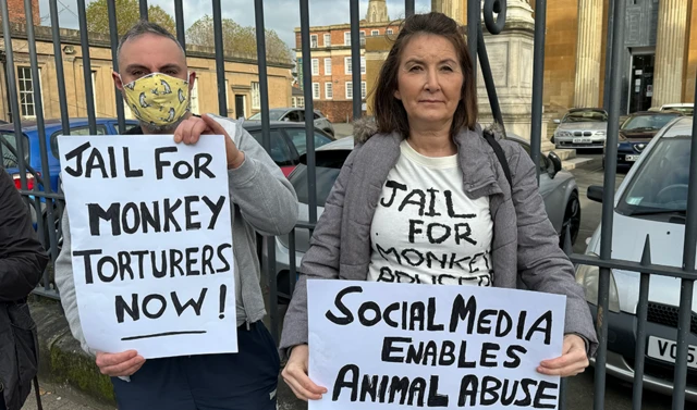 Two people holding placards saying: "Jail for monkey torturers now" and "Social media enables animal abuse"