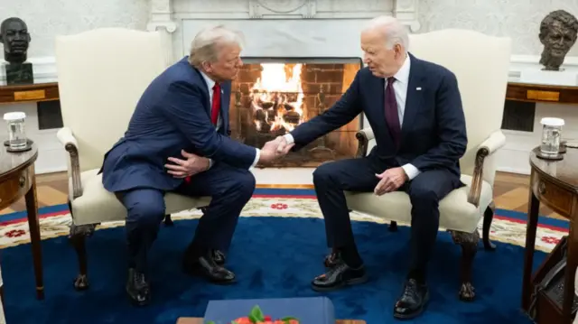 Joe Biden and Donald Trump shake hands in front of a roaring fire in the White House