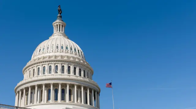 White marble exterior of the United States Capitol dome, with an American flag flying on a pole